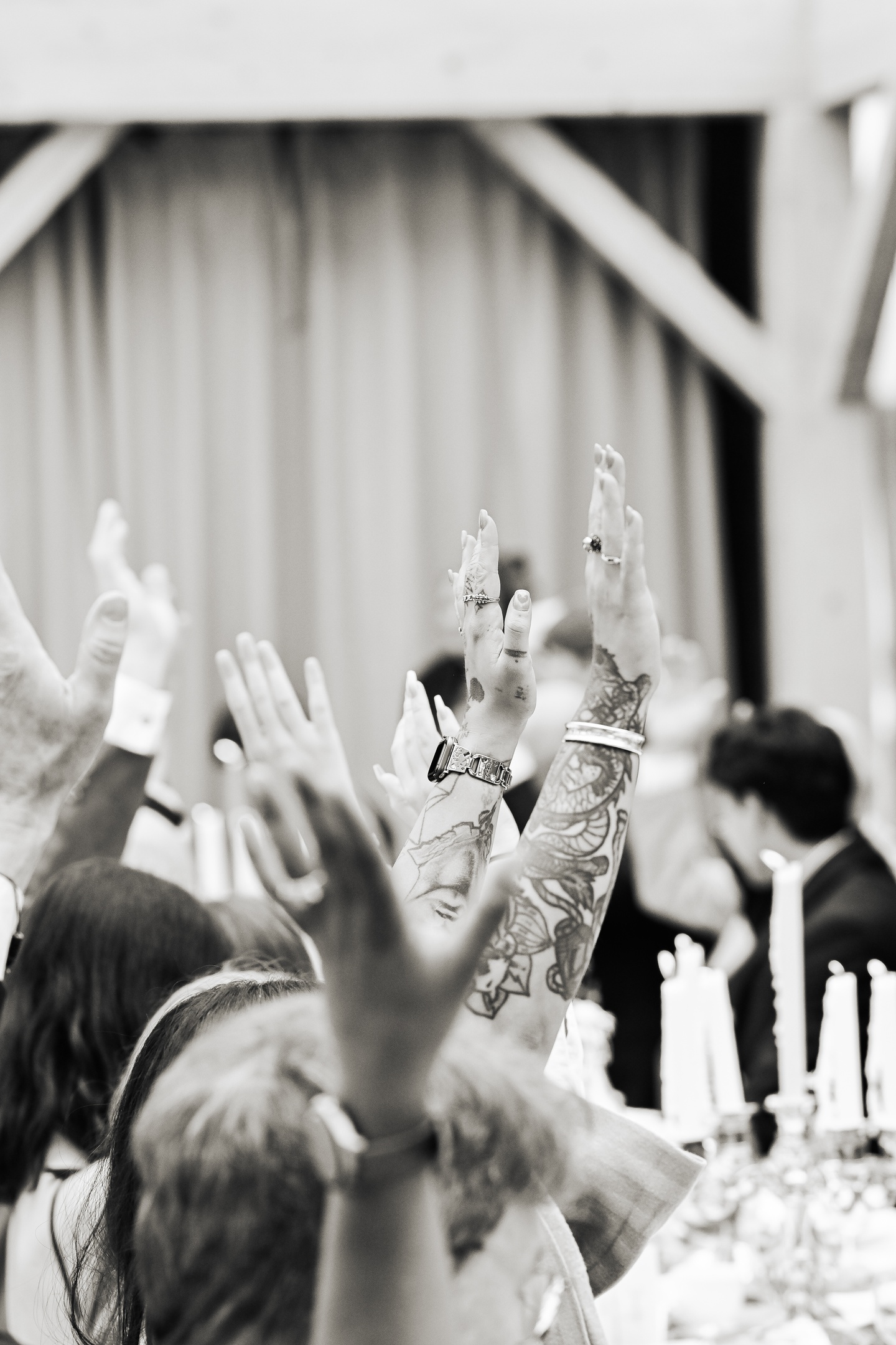 wedding guests raising their hands at the reception, guest with tattooed arms visible